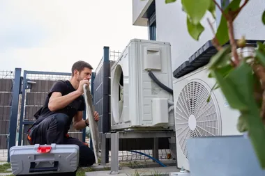 Technik serwisuje zewnętrzną jednostkę klimatyzacji przy domu.