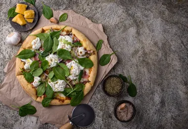 Pizza ze szpinakiem, serem i ziołami na papierze, z dodatkami obok.